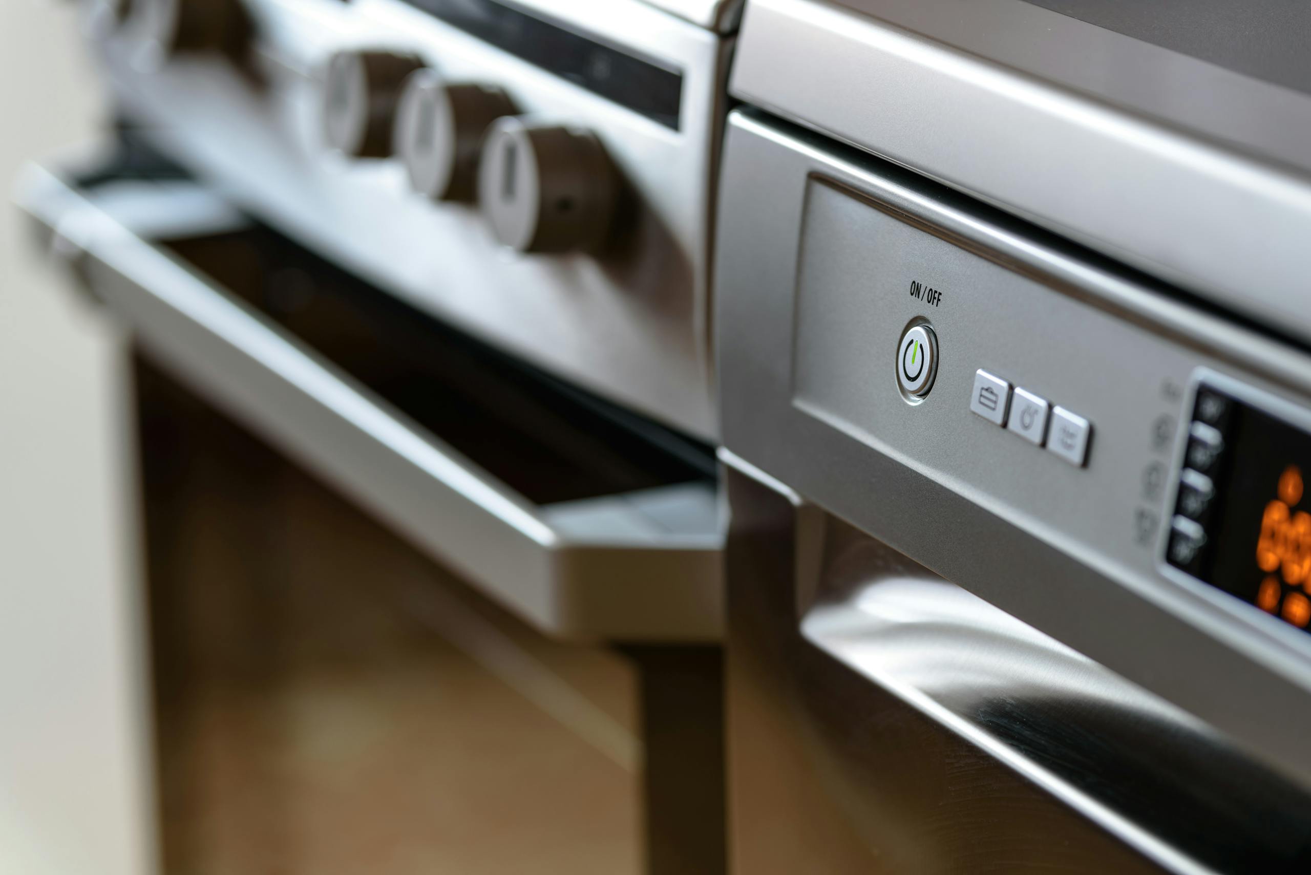 About Us Close-up view of modern stainless steel kitchen appliances with focus on dishwasher and oven.
